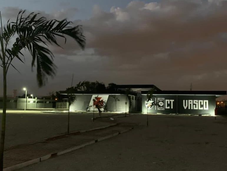 Fachada noturna do CT do Vasco iluminada, com os logos do clube e do projeto #NossoCT em destaque.