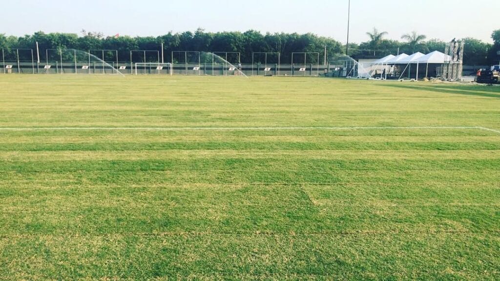 Campo de futebol do CT do Vasco com gramado verde e sistema de irrigação em funcionamento.