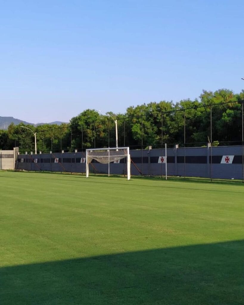 Campo de treino do CT do Vasco com o muro personalizado com a Cruz de Malta ao fundo.